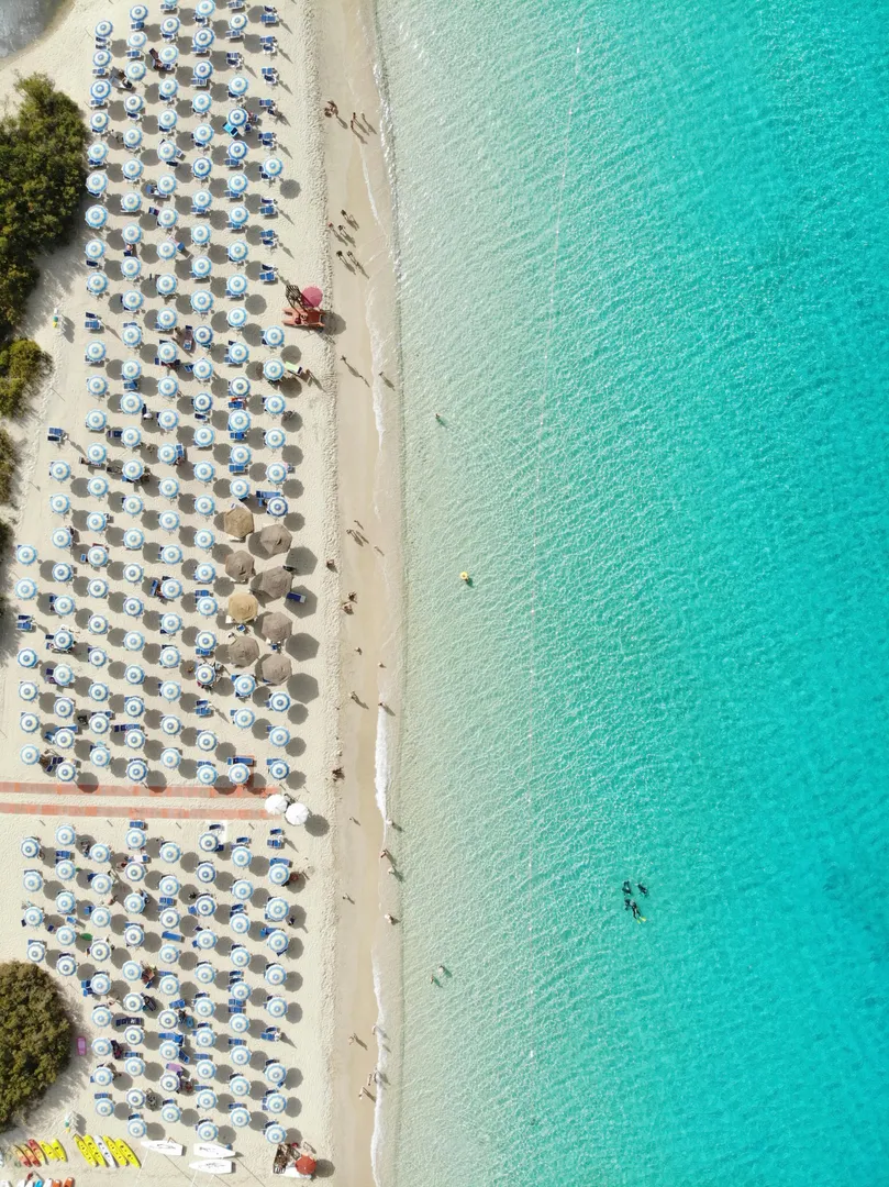 Aerial view of neat rows of beach umbrellas and loungers lining a Mediterranean shoreline