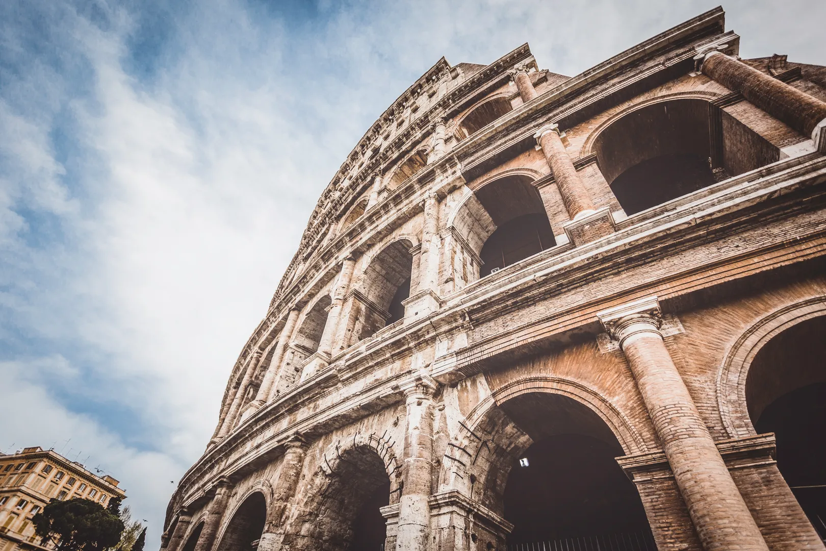 Low-angle view of the Colosseum's ancient arches and travertine facade against a blue sky in Rome